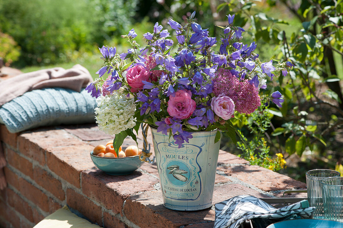 Sommerstrauß aus Glockenblumen, Rosen, Hortensie und Spornblume auf Gartenmauer