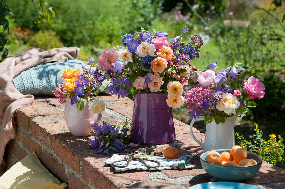 Colourful summer bouquets of roses, cranesbill, bluebells, spur flowers and oregano flowers on a garden wall