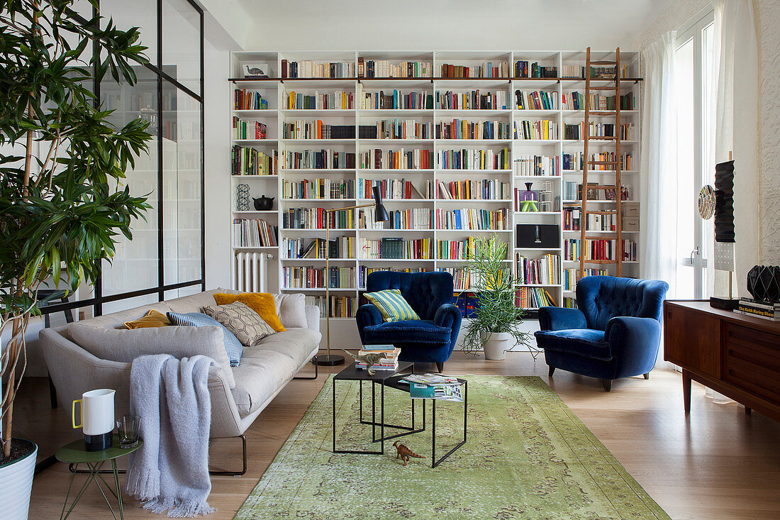 Floor-to-ceiling bookcase, sofa and blue velvet armchairs in eclectic living room