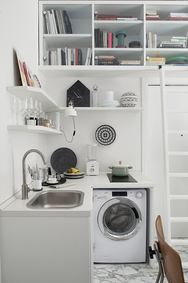 Washing machine in small kitchen below shelves in studio apartment