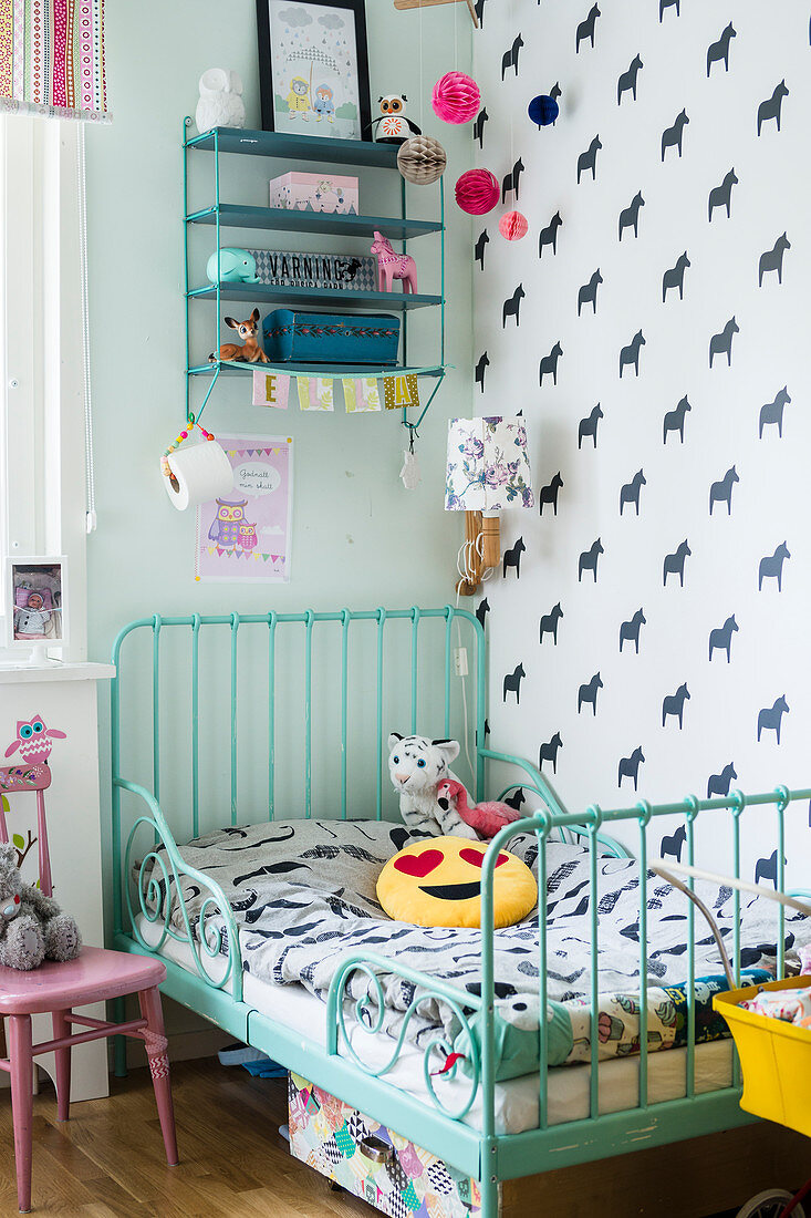 Turquoise metal bed in child's bedroom with horse-patterned wallpaper