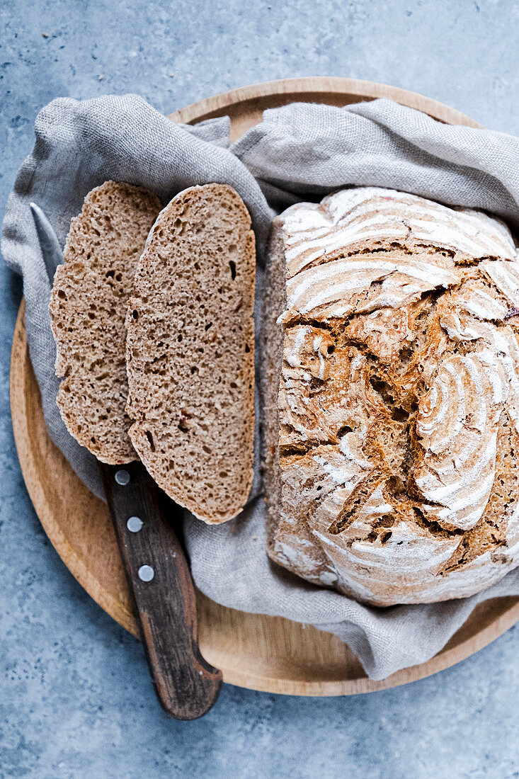 Sauerteigbrot, angeschnitten mit Messer auf Holzteller