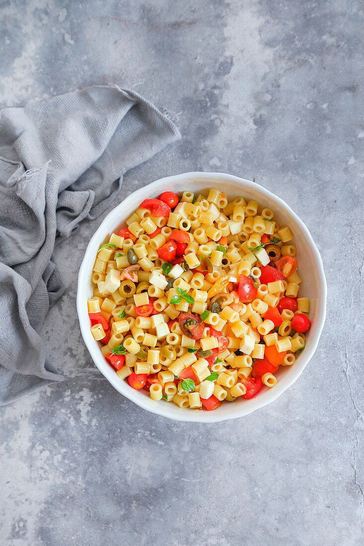 Cold pasta with mozzarella cherry tomatoes capers olives and aromatic herbs