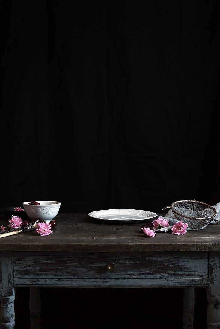 A fruit bowl, plate, sieve and blossoms on a wooden table