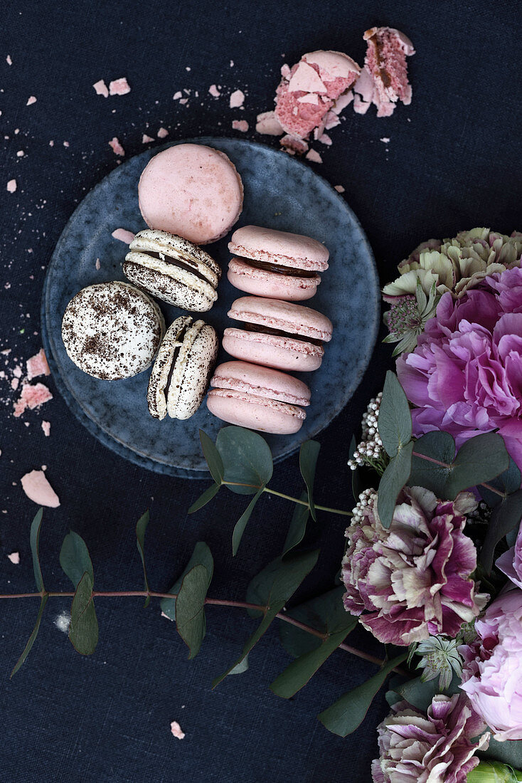 Two kinds of macarons on plates, beside peony blossoms