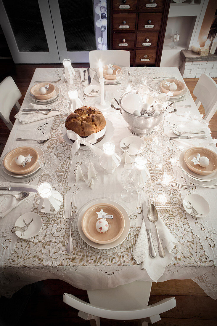 Top view of table festively set in white with lace tablecloth and tealight holders