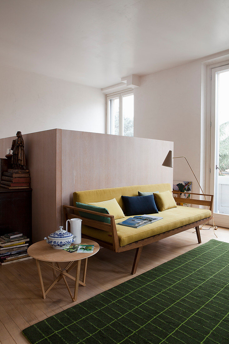 Gelbes Retro-Sofa mit Beistelltisch und grünem Teppich vor halbhoher Holzstellwand
