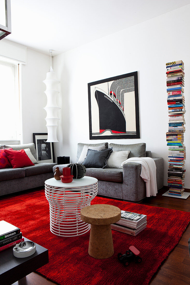 Wohnzimmer mit grauer Couch, Bücherturm-Regal und rotem Teppich als Farbakzent
