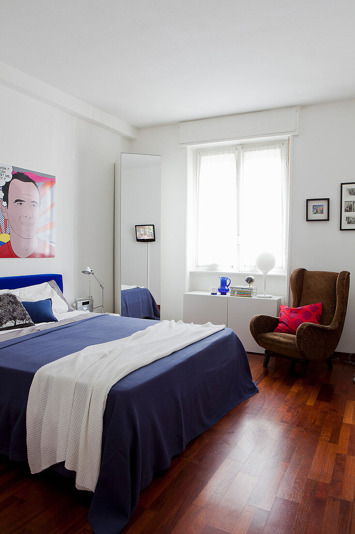 Schlafzimmer mit weißen Wänden, Pop-Art-Wandbild und blauem Bett als Farbakzent