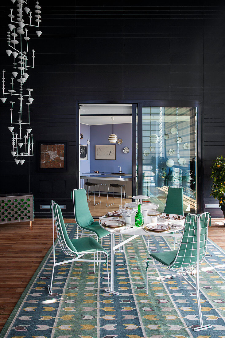 Interior of penthouse apartment with black walls, white metal furniture in dining area and blue and green rug