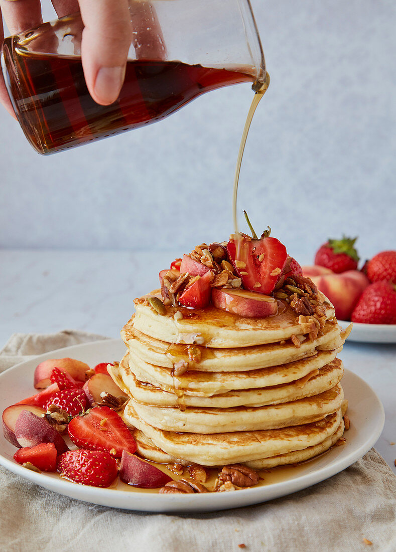 Pouring Maple Syrup Over A Stack of American Pancakes with Stawberries and Peaches