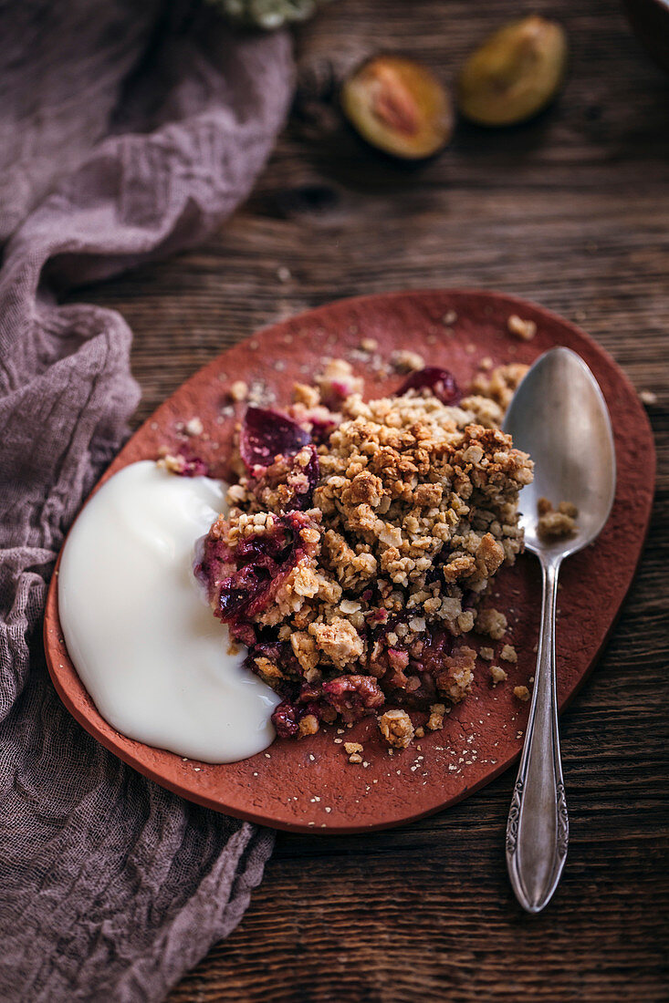 Plum crumble served with yogurt on a ceramic plate