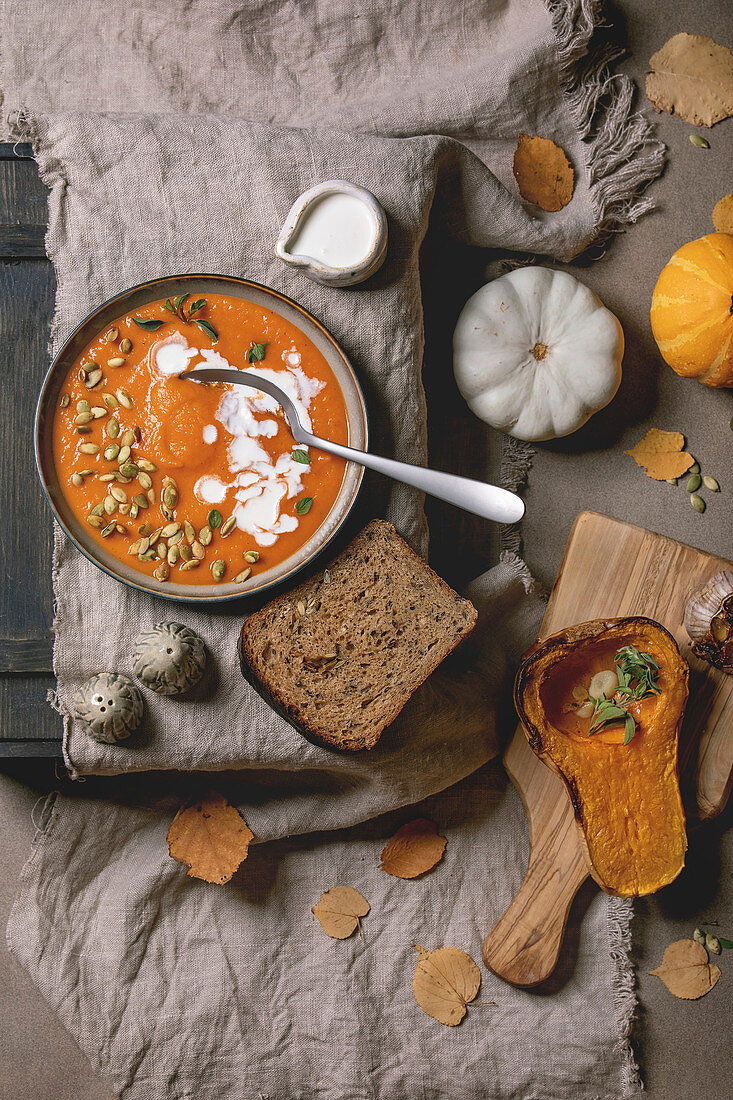 Pumpkin soup with cream and seeds in ceramic bowl on linen cloth, served with rye bread