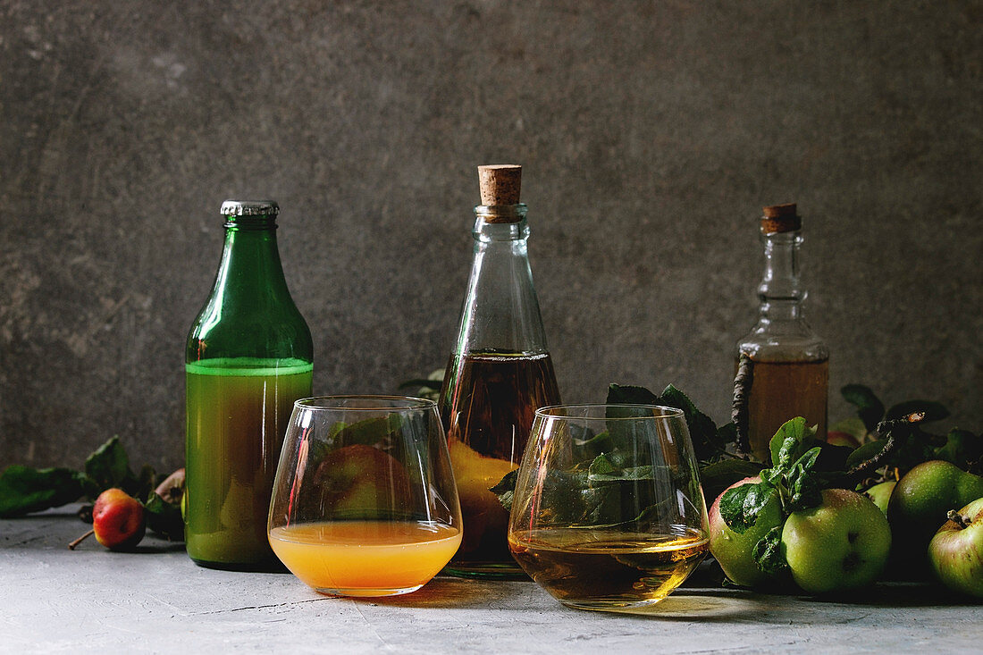 Bottles ang glasses of apple juice, vinegar and cider with garden apples with leaves and branches