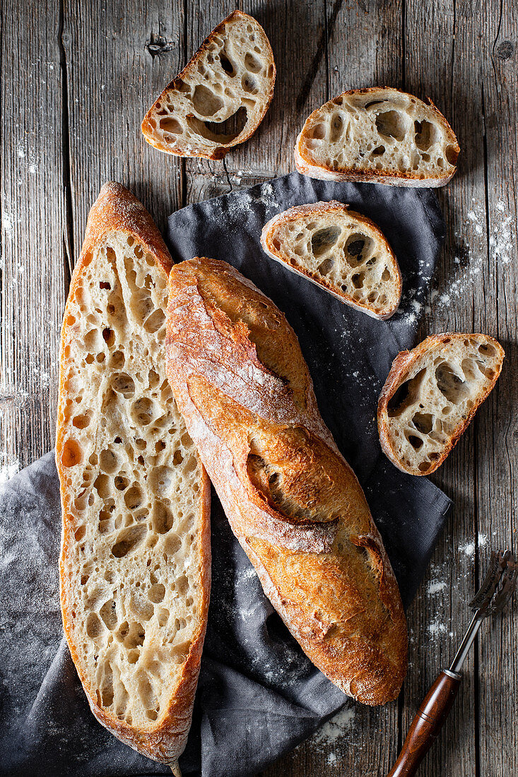 From above whole and halved appetizing baguettes arranged on white towel against rustic wooden background