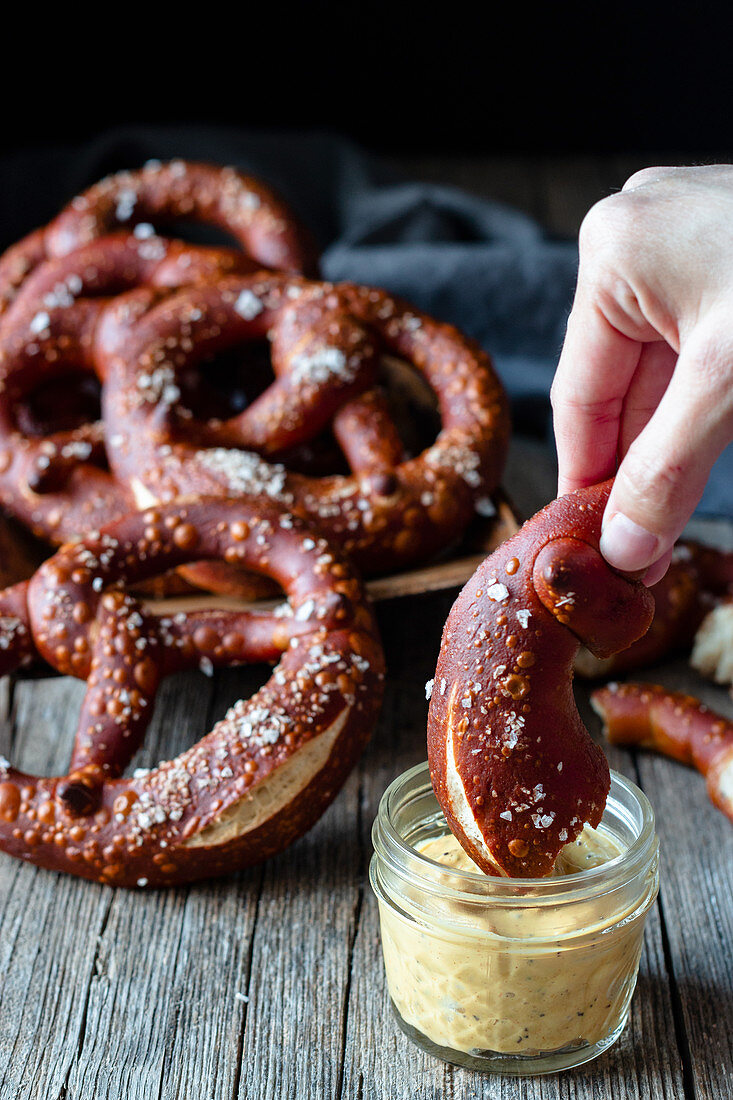 Crop person dipping homemade fresh pretzel with salt in cheese sauce on wooden table