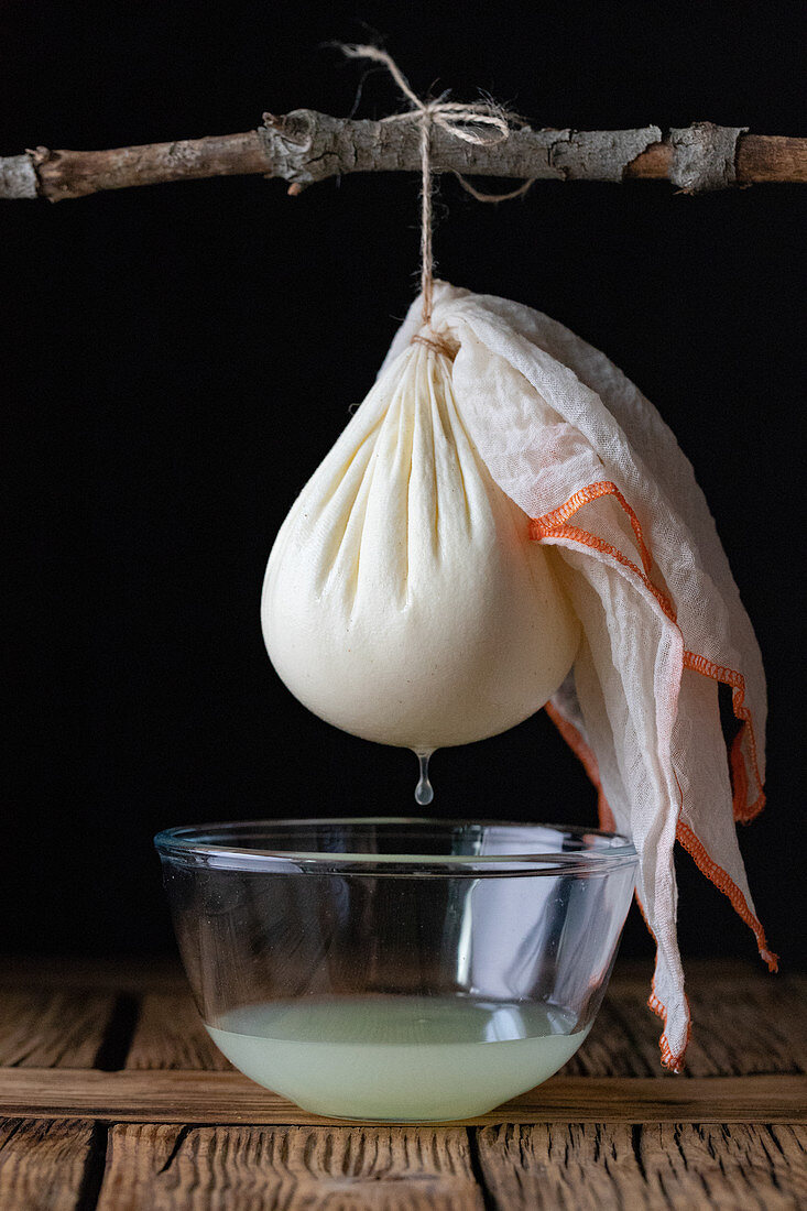 Cloth with ball of fresh labneh cheese hanging on twig over bowl with liquid