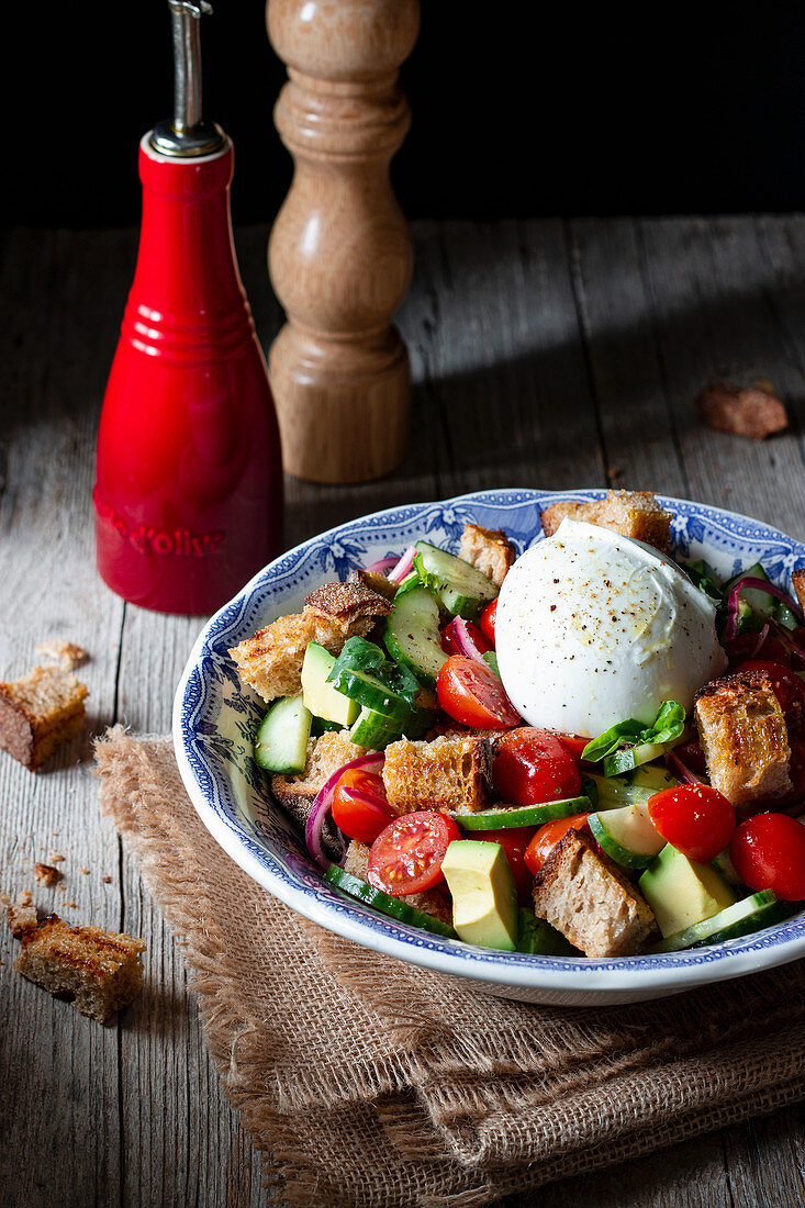 Bowl with yummy panzanella salad placed on cloth on wooden table against black background