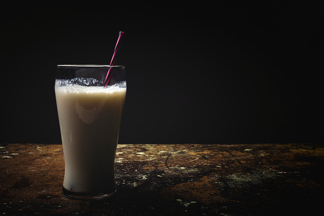 Tall glass of white milk with bright striped straw on table over black background