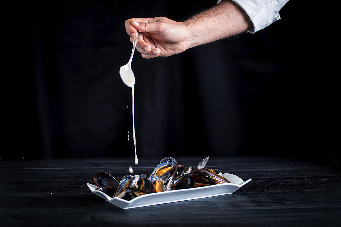 Crop cook pouring fragrant appetizing mussels with Thai sauce on black background