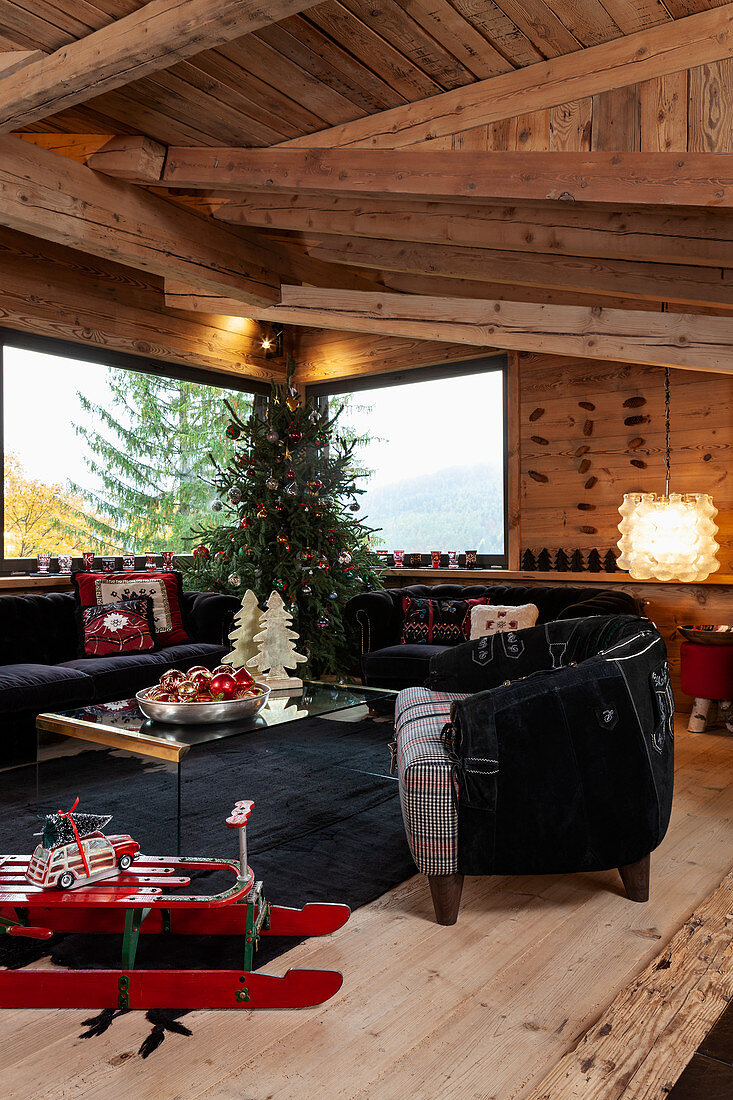 Red sledge, black sofa set and decorated Christmas tree in living room of chalet