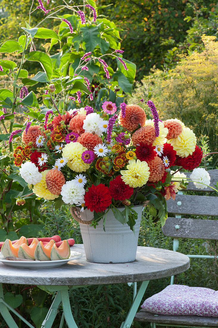 Strauß aus Dahlien, Zinnien, Sonnenbraut, Knöterich und Aster, Teller mit aufgeschnittener Melone