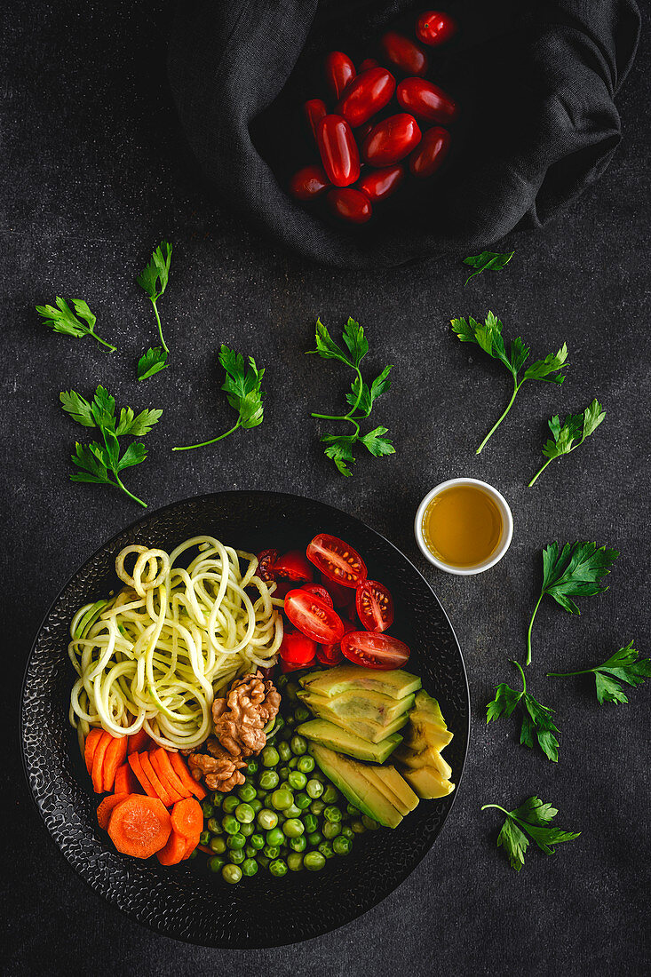 Zucchinispaghetti mit Erbsen, Kirschtomaten und Avocado in einer Schale