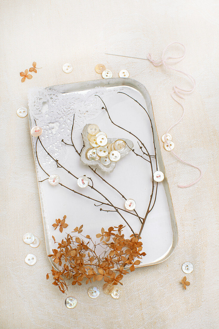 Blechdose dekoriert mit Zweigen, Spitzenstoff und Schmetterling aus Perlmuttknöpfen
