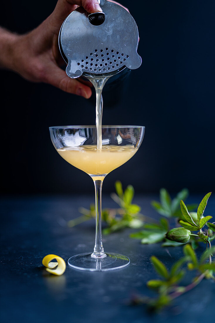 Cocktail 'Corpse Reviver' wird durch Barsieb in Cocktailglas gegossen