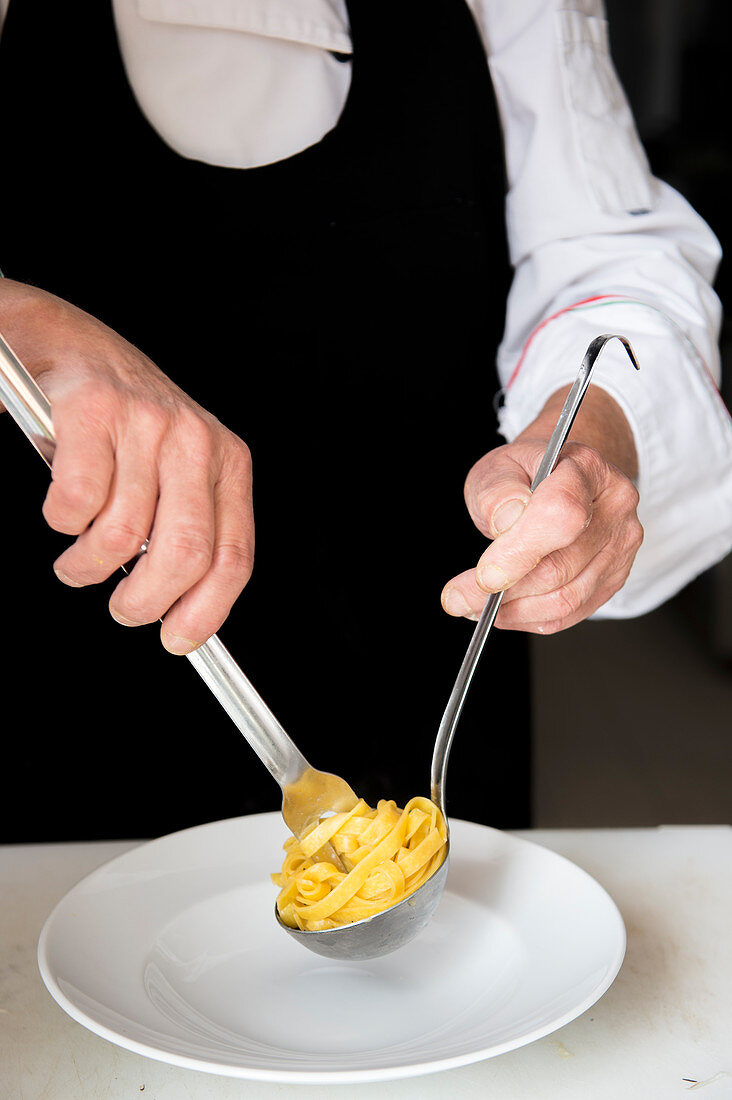 Professional chef arranging cooked fettucine pasta on a white plate
