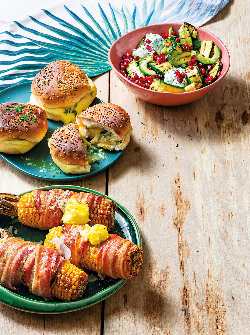 BBQ-Beilagen - Zucchinisalat, Grillbrötchen und mit Speck umwickelte Maiskolben