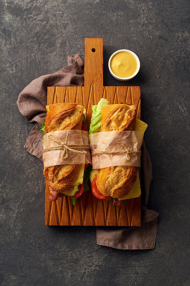 Baguette sandwich with bacon, chedder cheese, mustard, lettuce and vegetables