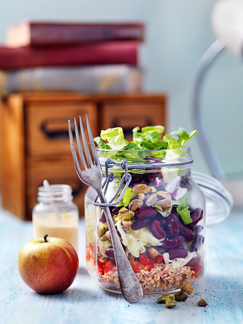 Vegeterian lunch salad in a jar with apples, beans, red pepper, pistachios and bulgur