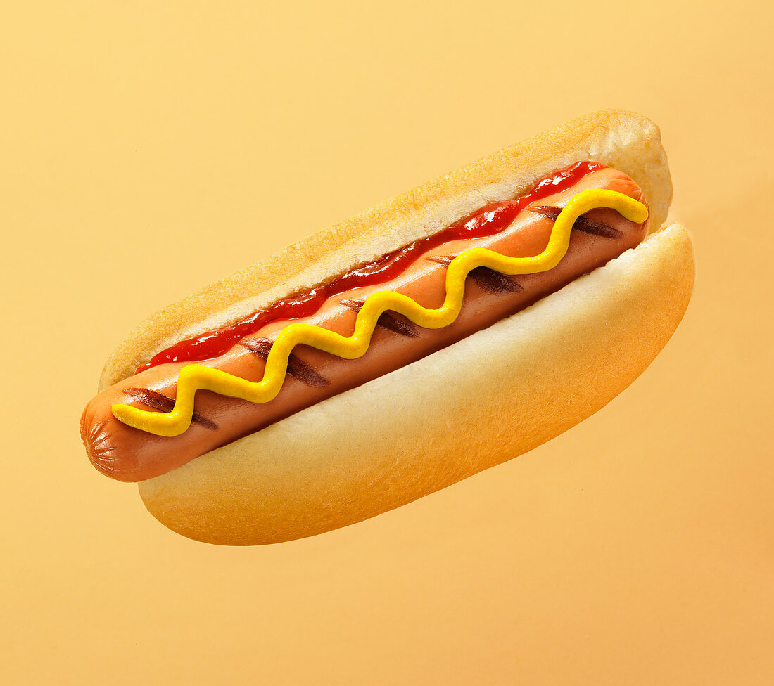 Ein gegrillter Hot Dog mit Senf und Ketchup vor farbigem Hintergrund