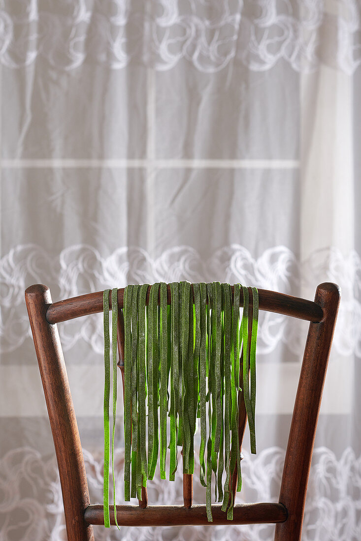 Homemade spinach pasta drying on a wooden chair