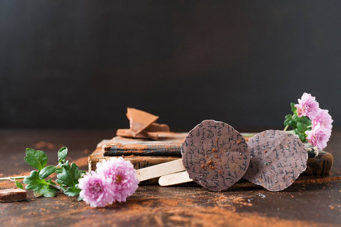 Schokoladenlollies und Asternblüten vor dunklem Hintergrund