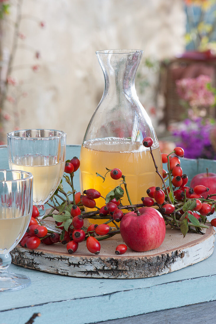 Decanter and glasses with apple juice, wooden slice as coaster, apple and rose hips as decoration