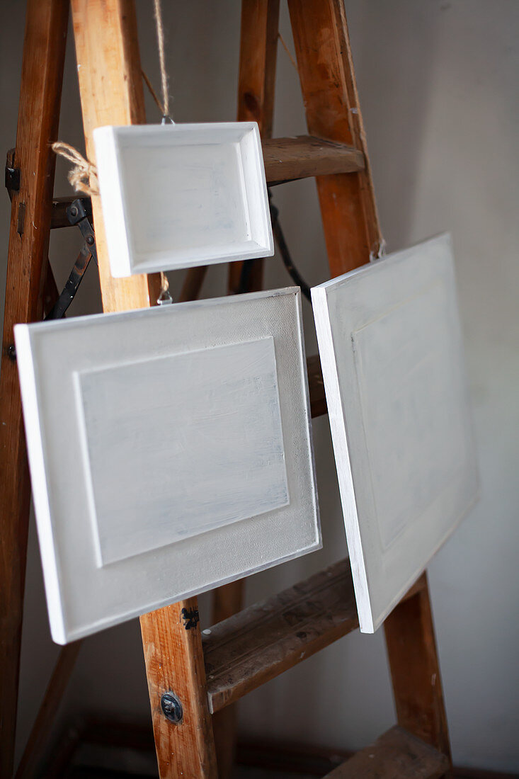 Framed pictures painted over in white hung from old wooden stepladder