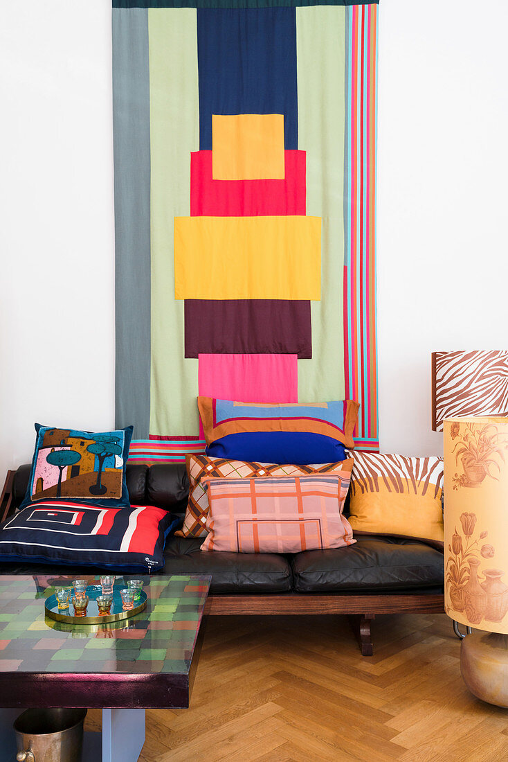 Scatter cushions on leather sofa below colourful wall hanging