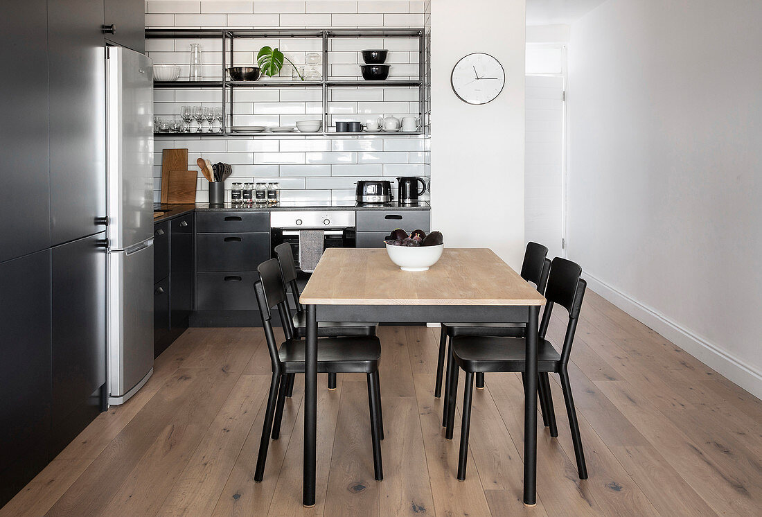 Dining table in kitchen area of apartment with open shelves above black worksurface