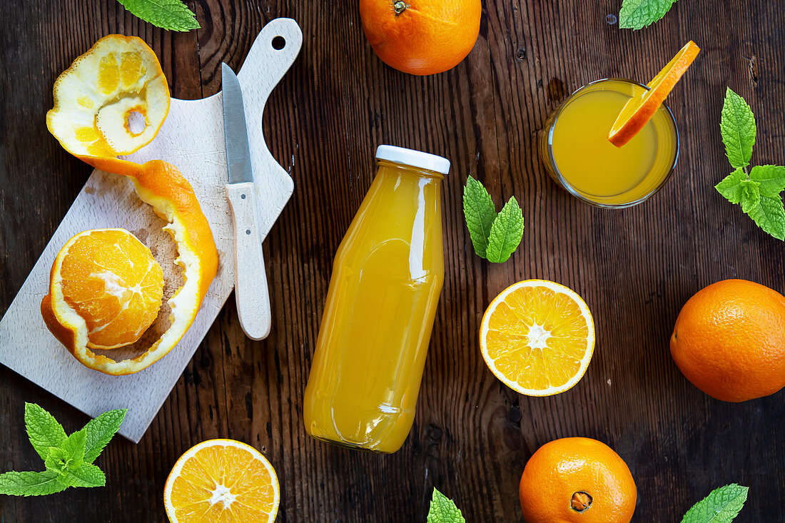 Orangensaft in Glas und Flasche mit frischen Orangen und Minzblättern