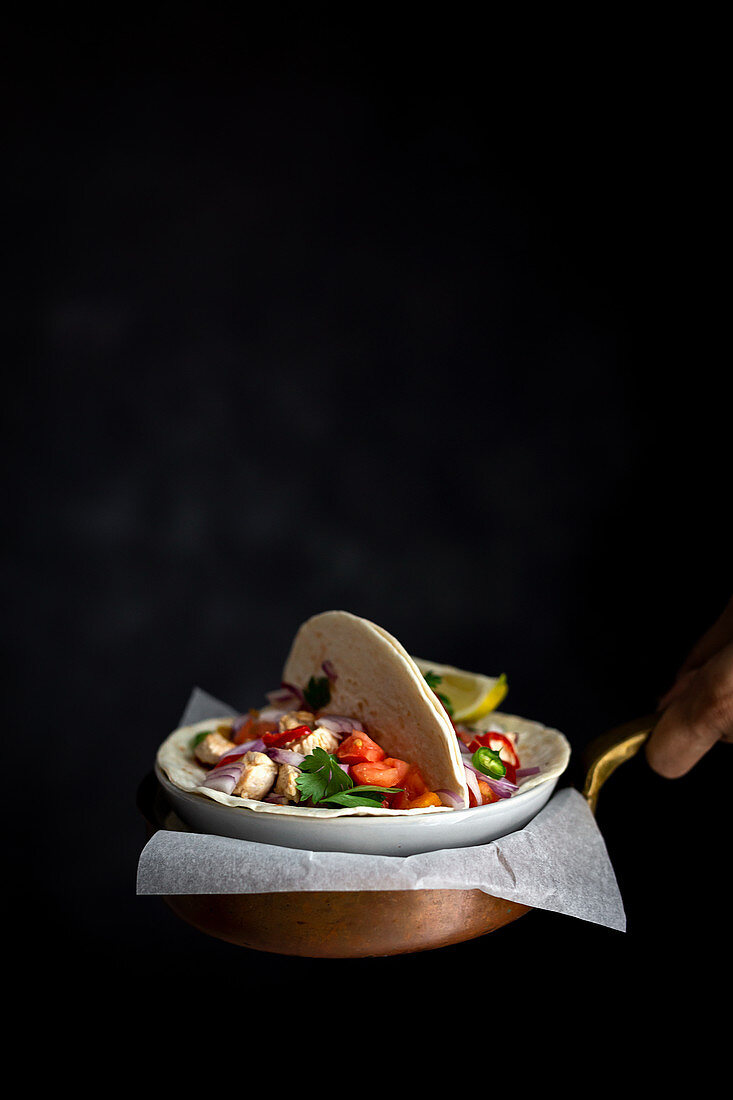 Hands holding Mexican Tacos with fresh vegetables and chicken on dark background