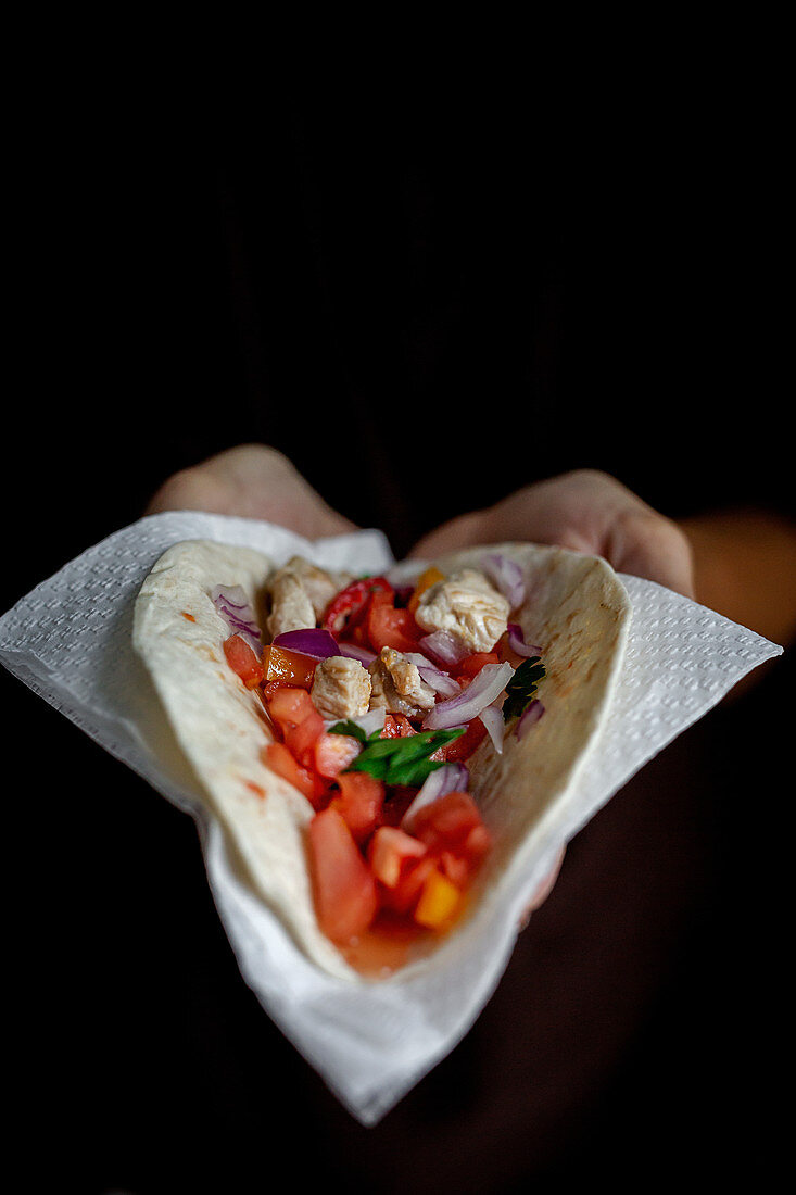 Hand hält Taco mit Hähnchen und Gemüse (Mexiko)