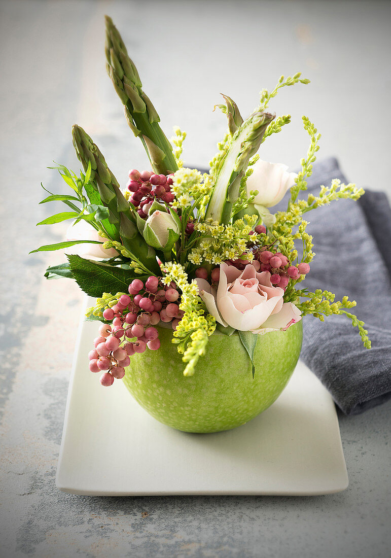 Frühlingsgesteck mit Rosen und Spargel in einem grünen Apfel