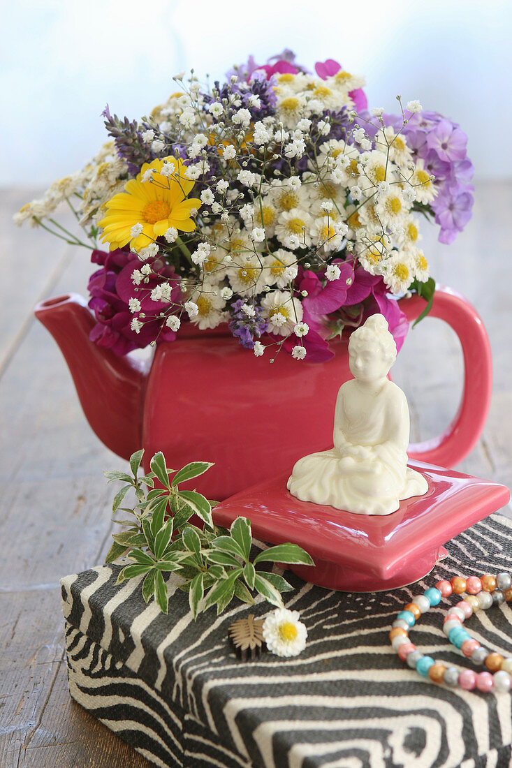 Summer bouquet in teapot next to Buddha figurine on teapot lid
