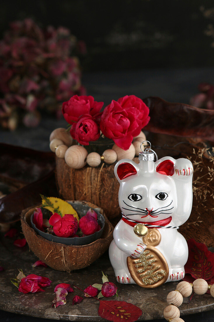 Tischdekoration mit Winkekatze und roten Rosen in Kokosnussschalen