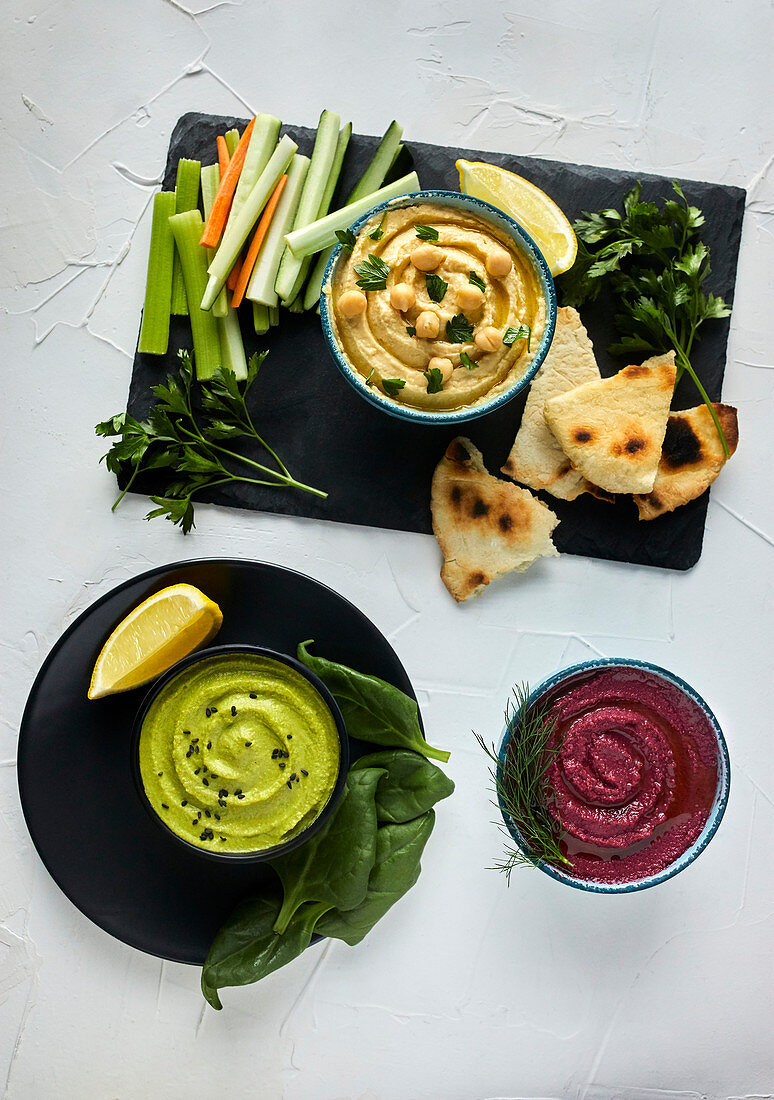 Various types of hummus served with fresh vegetables and pita bread