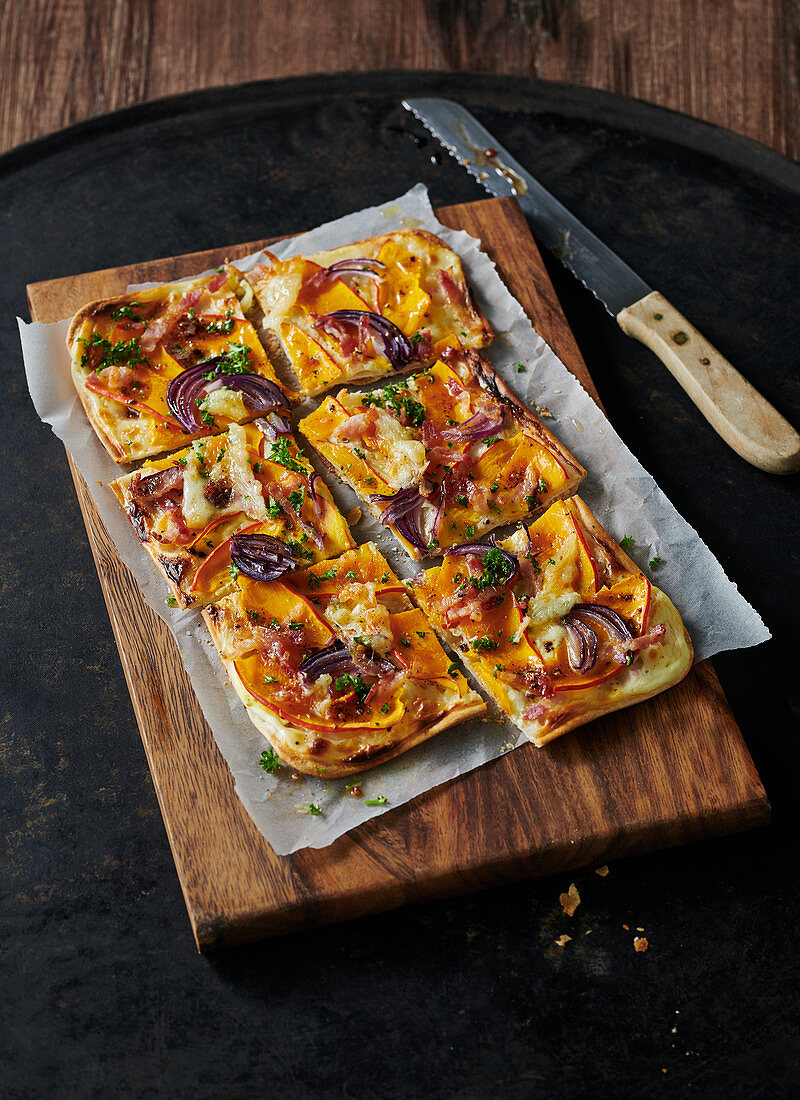 Tarte flambé with pumpkin and red onions on wooden board