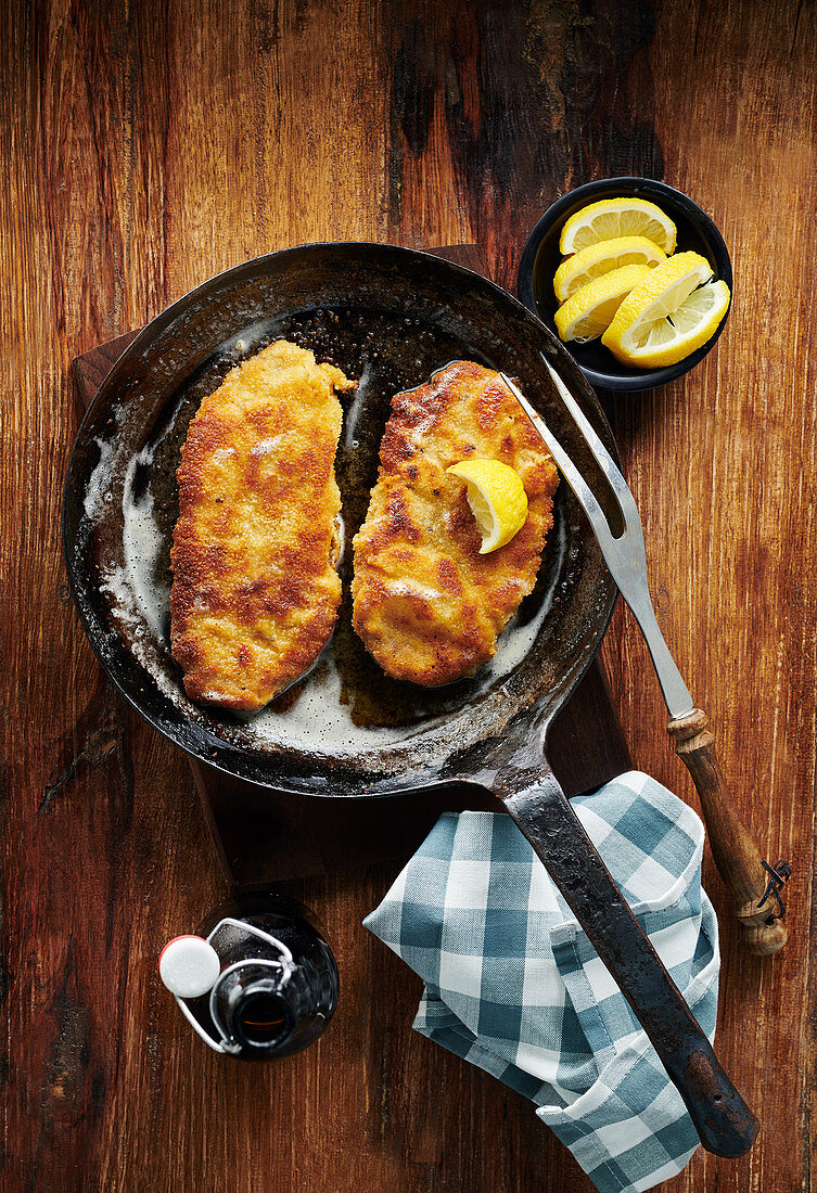 Wiener Kalbsschnitzel in rustikaler Gusseisenpfanne auf Holztisch