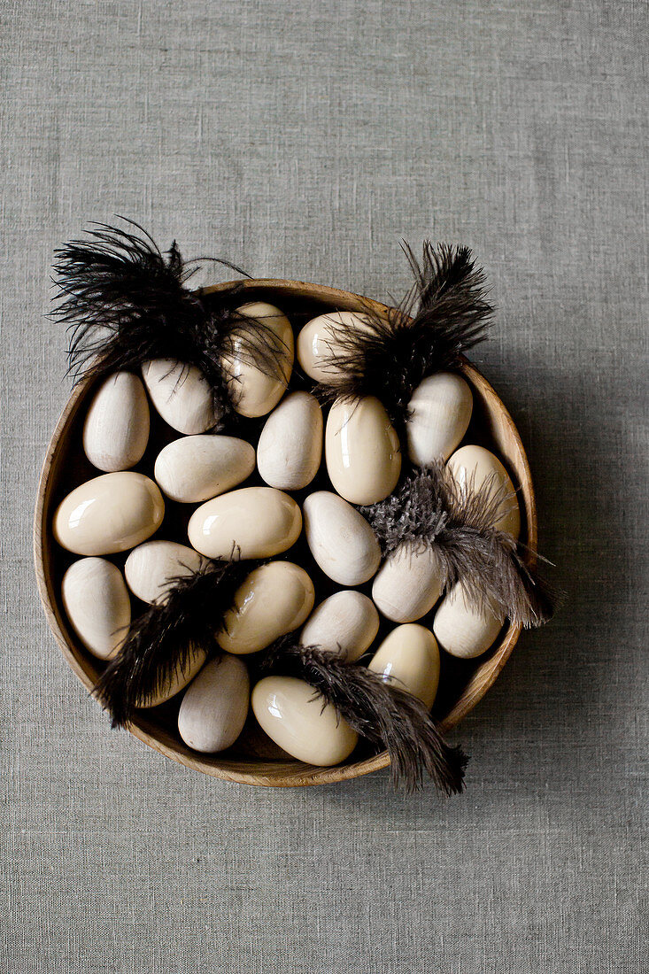 Wooden and ceramic eggs and brown feathers in wooden bowl